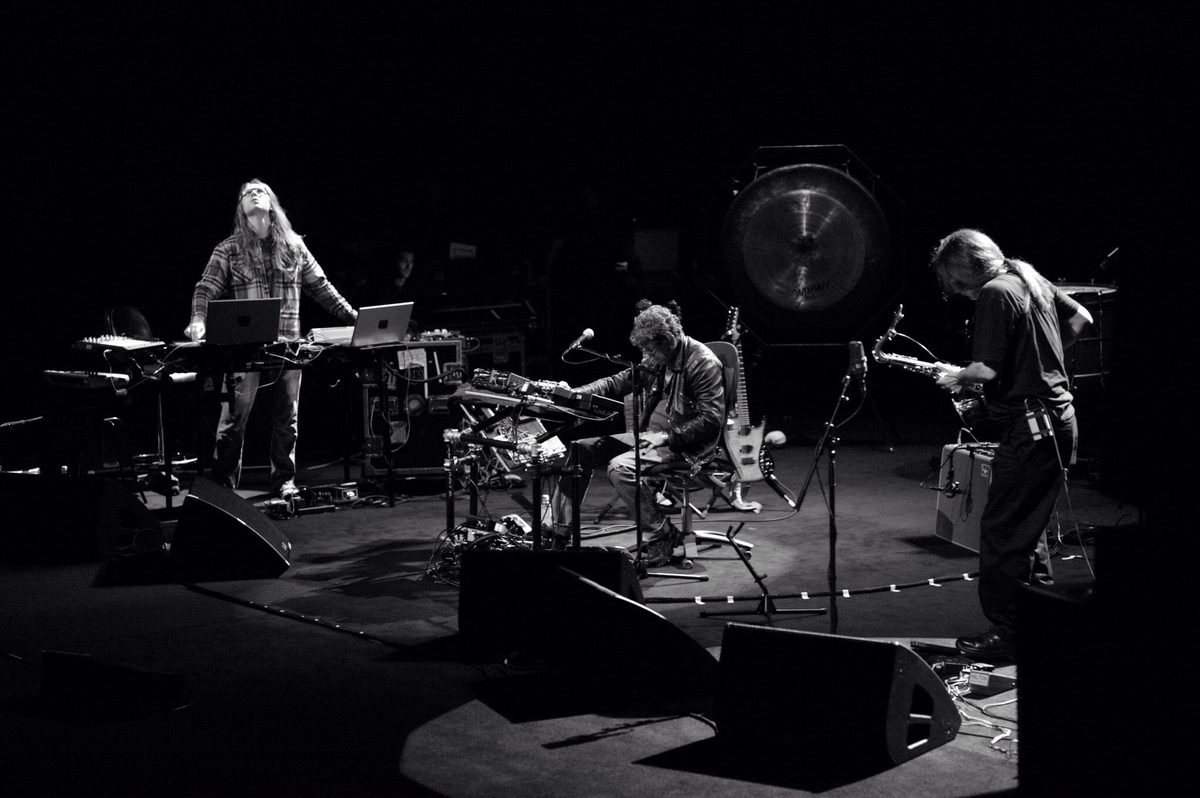 Metal Machine Trio on the Opera Theatre stage at the Sydney Opera House, in black and white: three players among laptops, amplifiers and speaker wedges, with a large gong behind them. Left to right: Sarth Calhoun, Lou Reed, Ulrich Krieger.